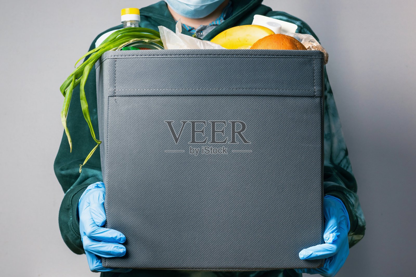 一个带着蓝色医用手套和口罩的快递员用灰色的盒子递送食物。照片摄影图片