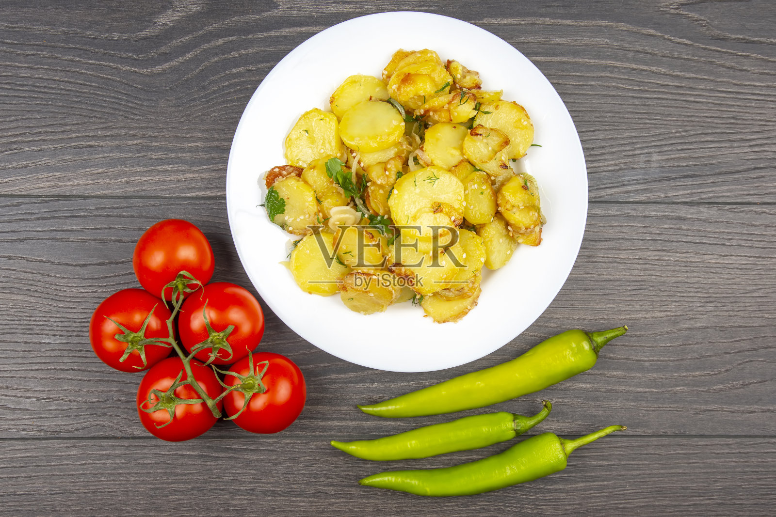 木桌上的白盘子里放着炒熟的土豆，配上香草和蔬菜照片摄影图片