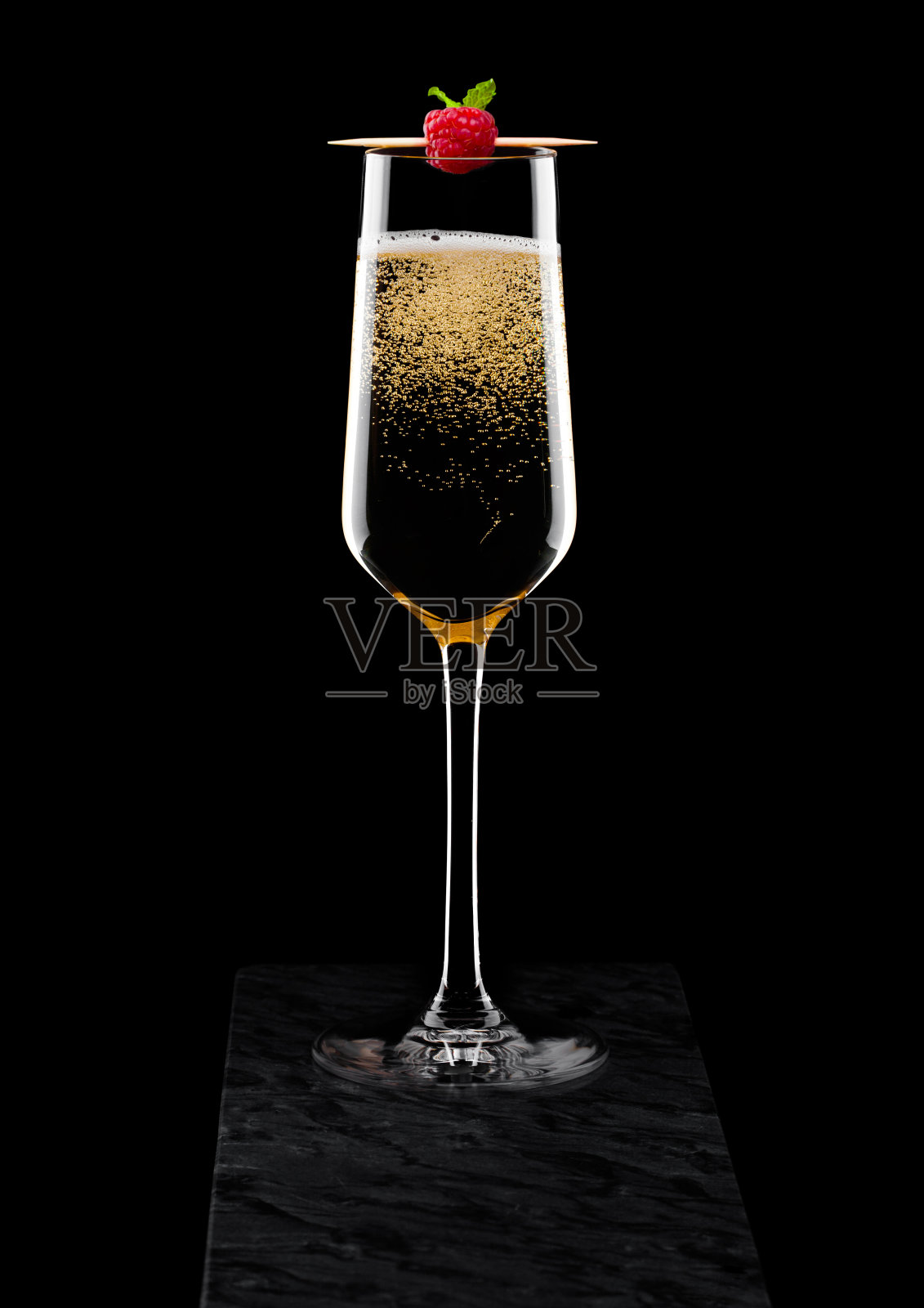 优雅的黄色香槟杯，在黑色的背景上的黑色大理石板上的棒子。照片摄影图片