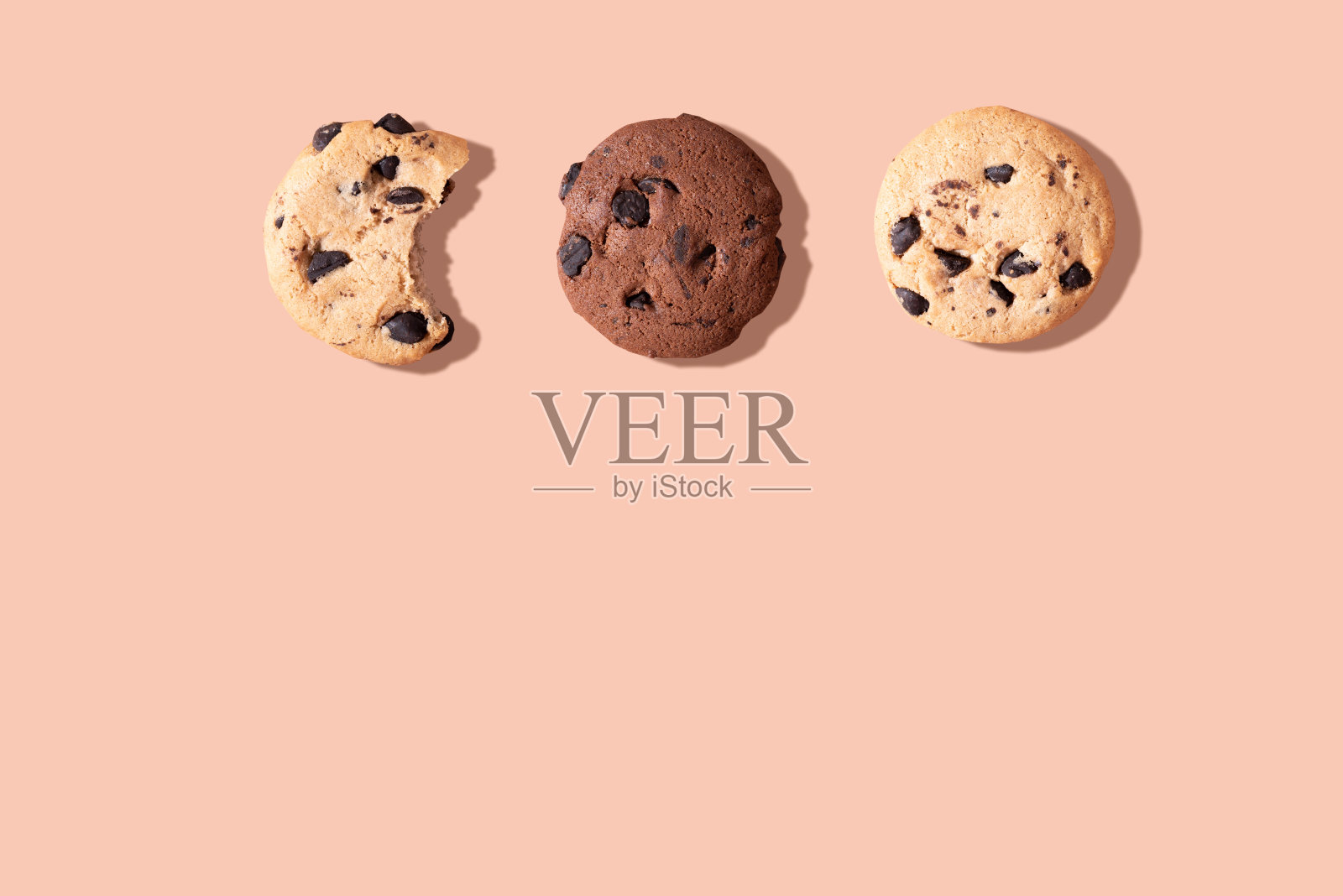 三块巧克力曲奇，一块被咬了，背景是棕色。照片摄影图片