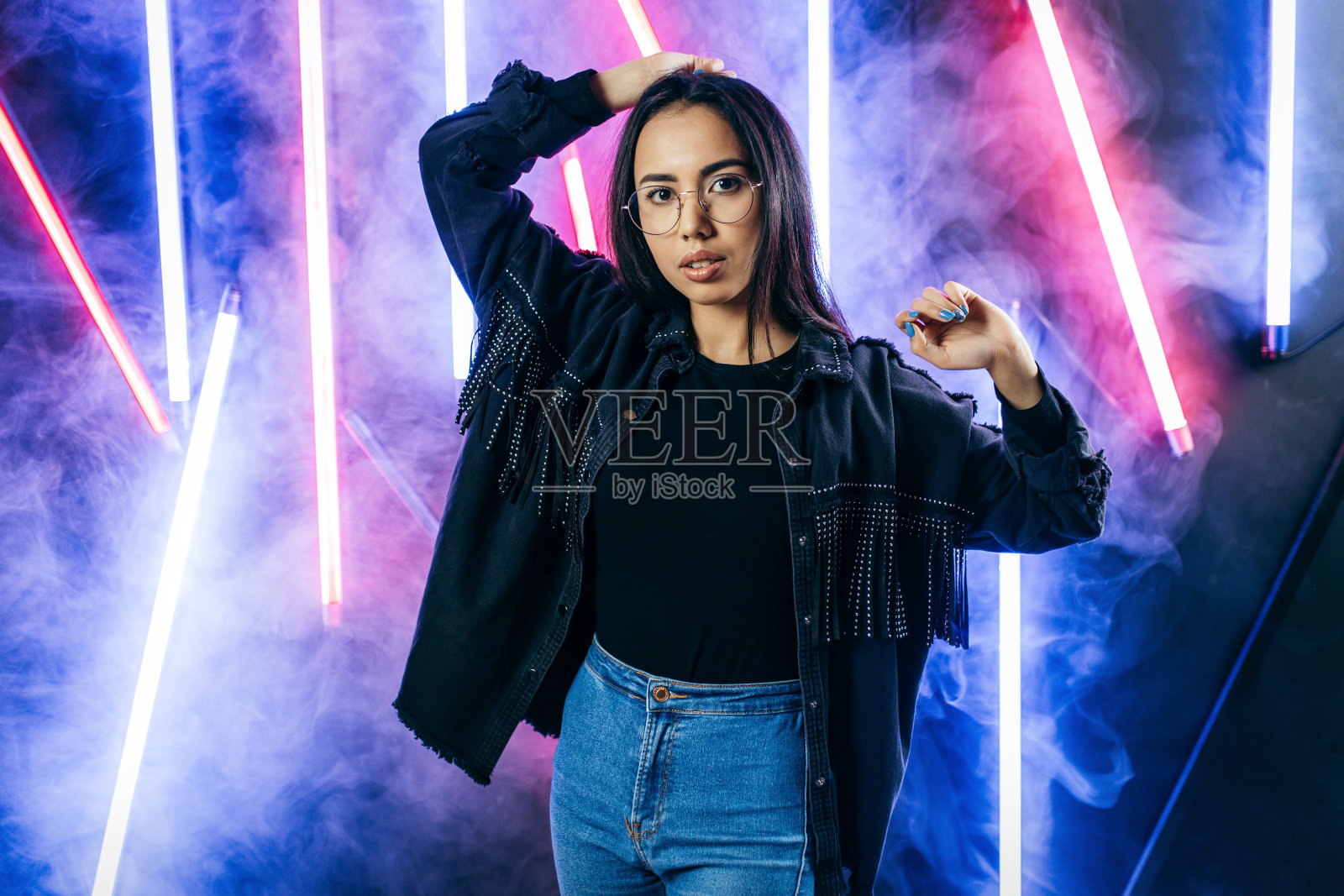 这是一幅时尚的年轻女子肖像，她戴着眼镜，穿着黑色t恤和棉质夹克，背景是烟雾中的霓虹灯照片摄影图片