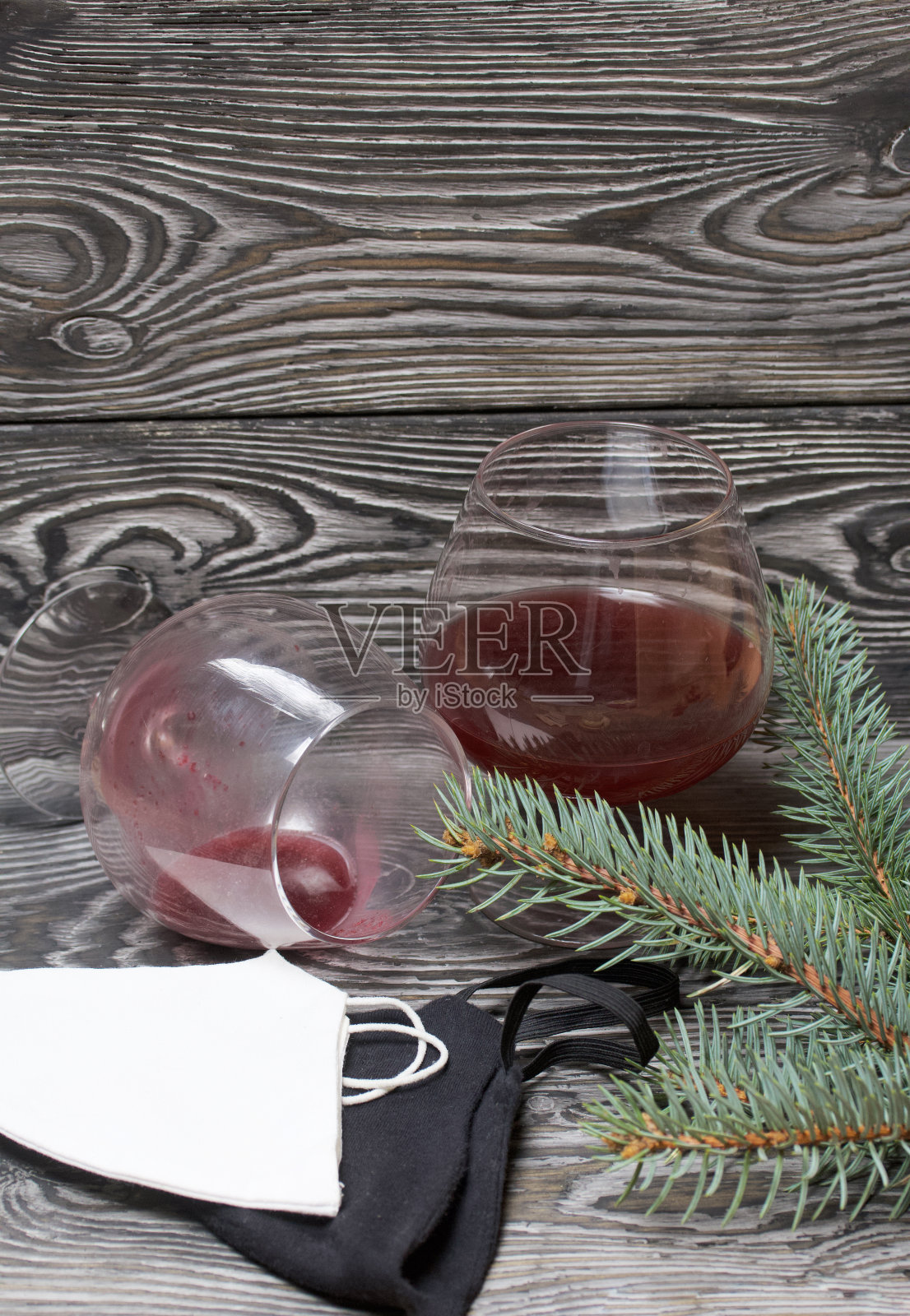 一杯红酒。又一个杯子被打翻了。附近有医用口罩和一根云杉树枝。松木板。照片摄影图片