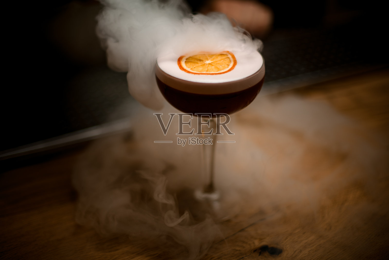 一杯泡沫饮料和一片柑橘放在烟雾缭绕的吧台上。照片摄影图片