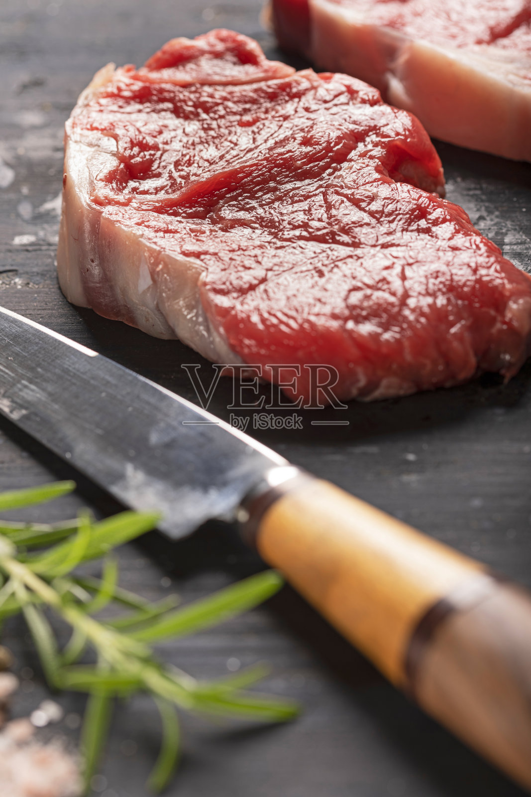 牛柳配刀把盐、胡椒和迷迭香放在黑色背景上照片摄影图片