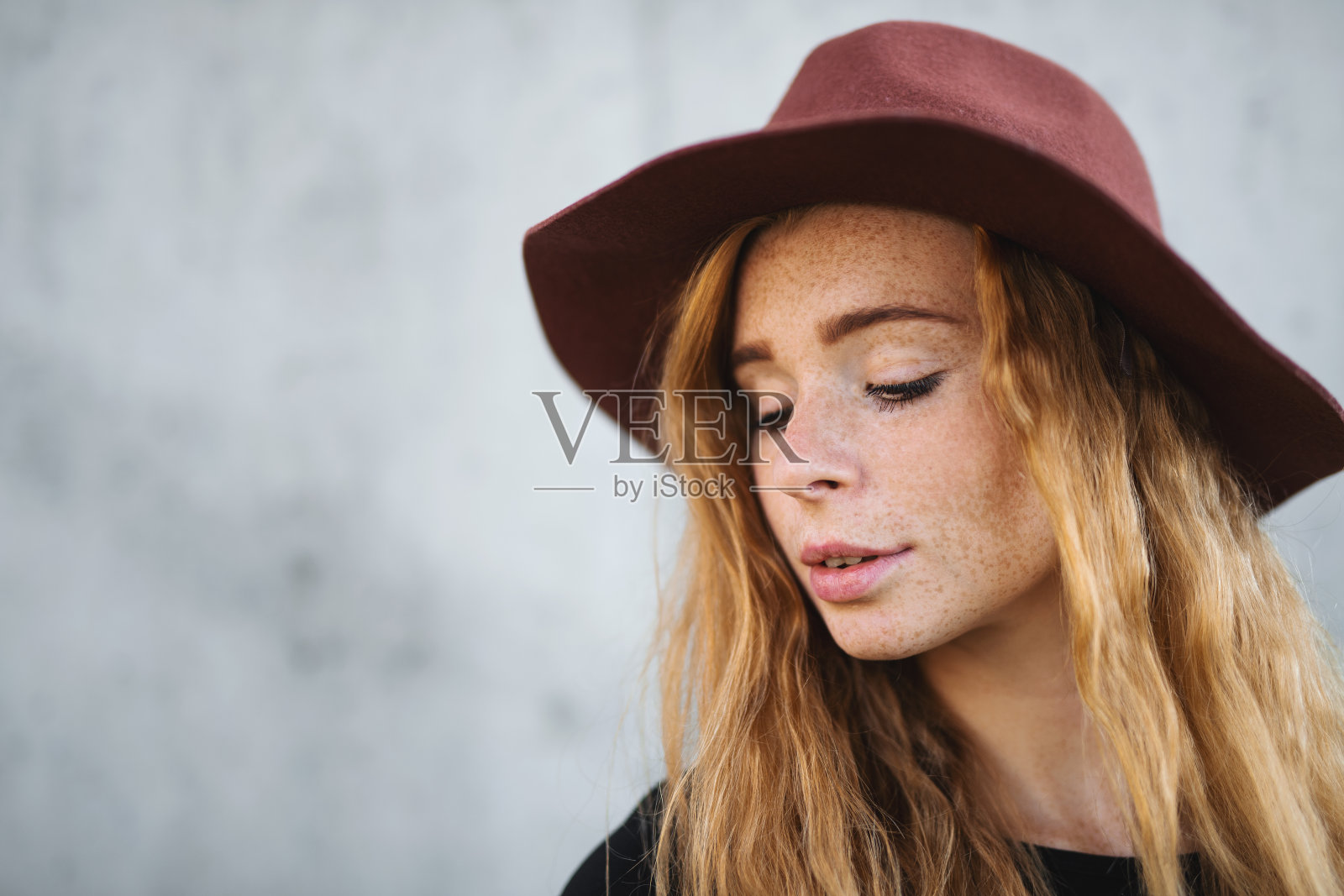 年轻女子的肖像与红色头发和帽子站在灰色的背景。照片摄影图片