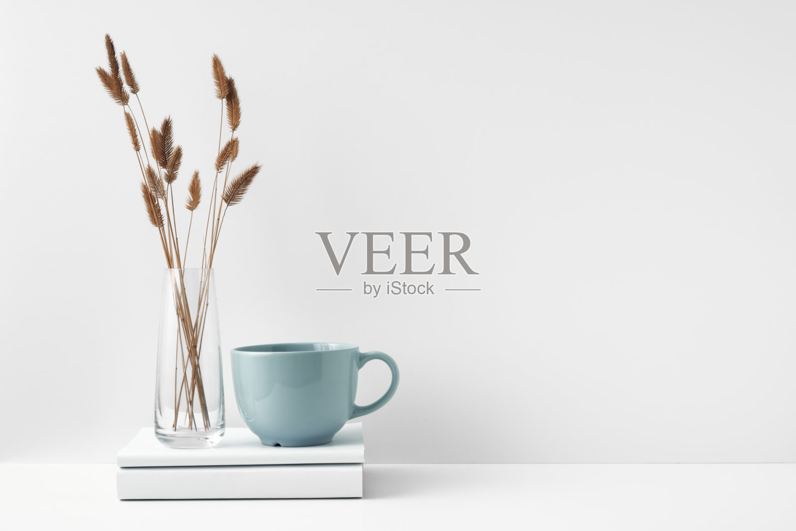 一个放在一堆书上的杯子和一个插着干花的透明花瓶。室内装饰采用环保材料，极简主义。复制空间，模拟。照片摄影图片