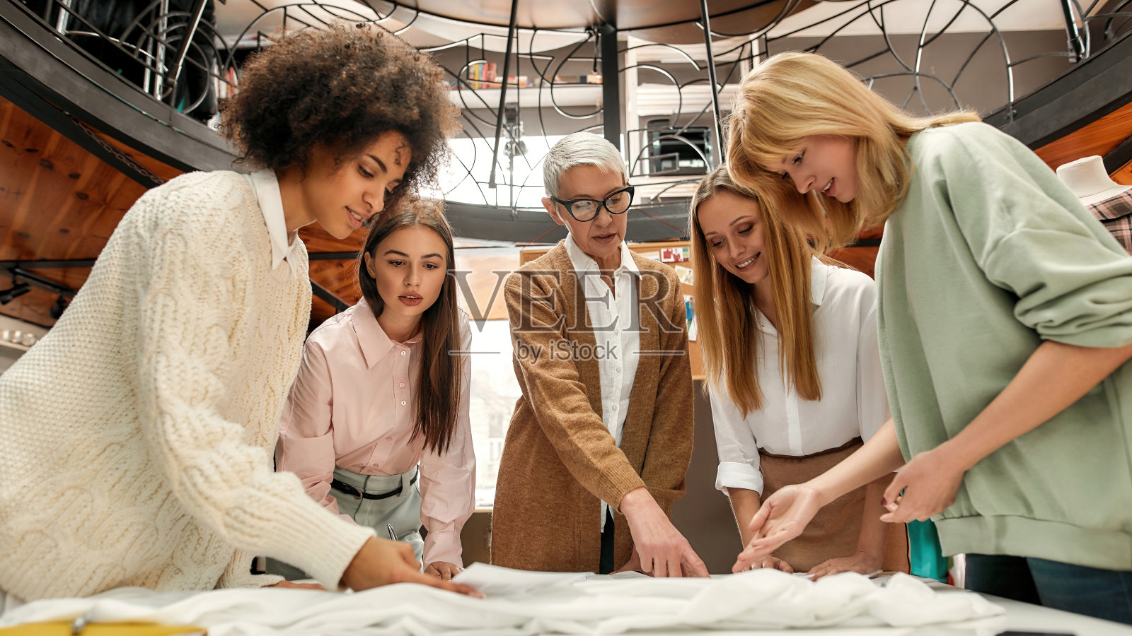 五名不同年龄、富有创意的女性穿着考究地围在一张桌子周围讨论她们的想法照片摄影图片