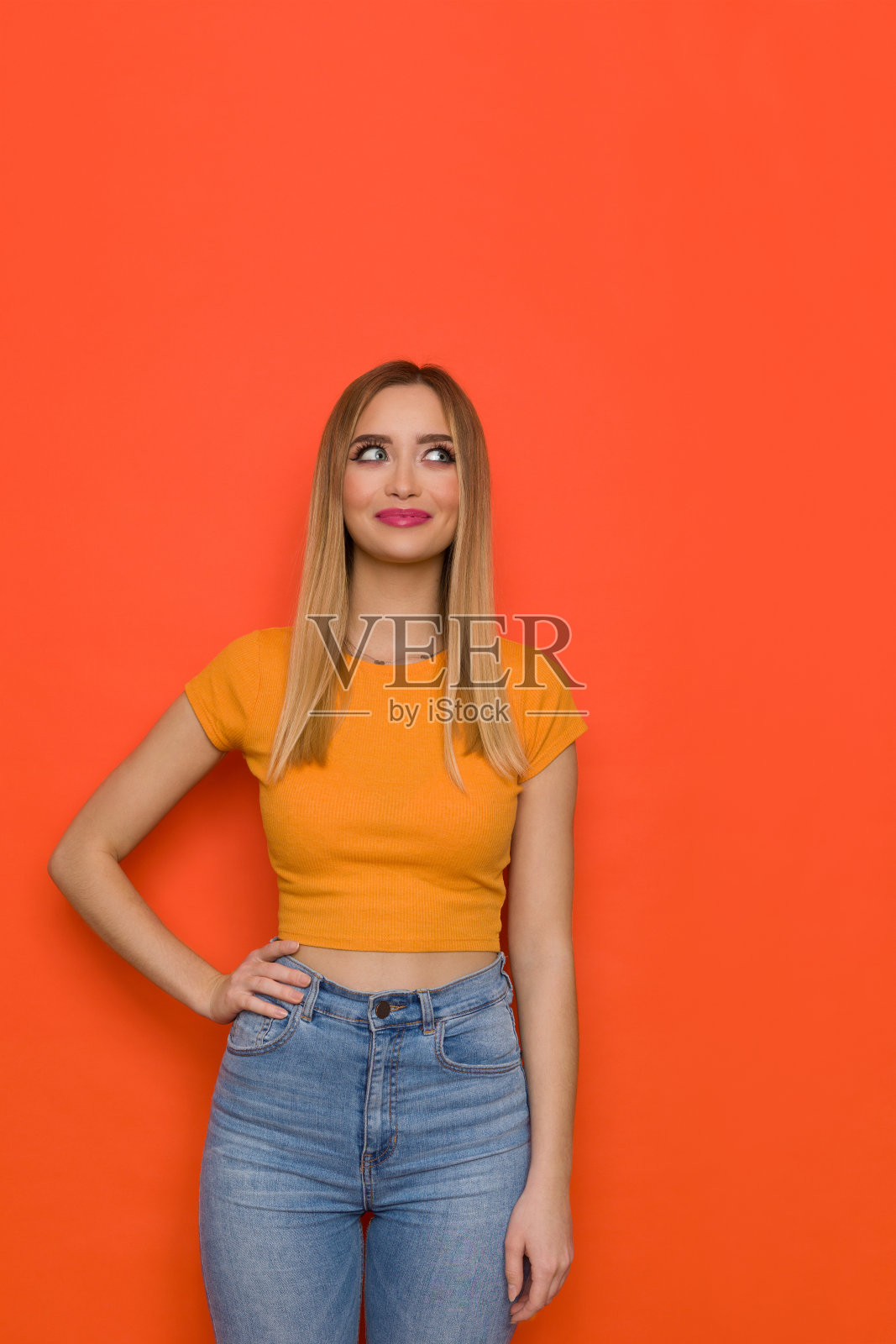 穿着橙色衬衫和牛仔裤的年轻女子微笑着看向别处照片摄影图片