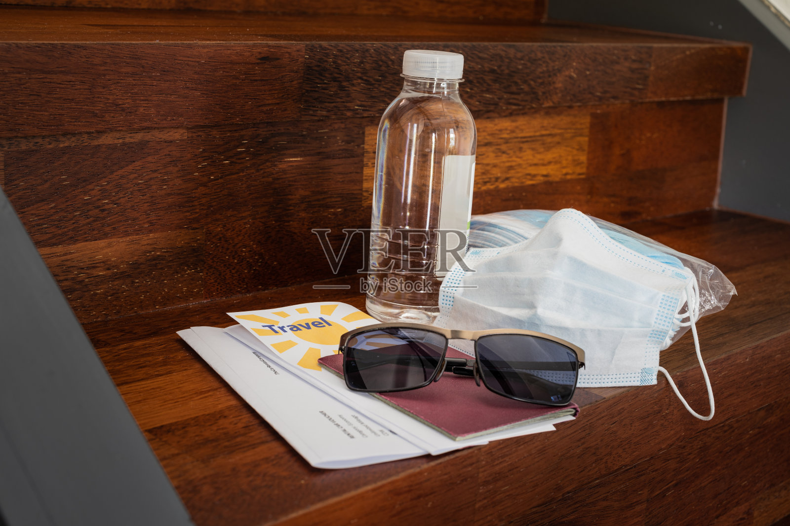 在冠状病毒概念时代旅行:准备好一包口罩、一个用过的口罩、一瓶消毒剂、一本护照、旅行证件、太阳镜和旅行证件，放在楼梯上准备出发。照片摄影图片