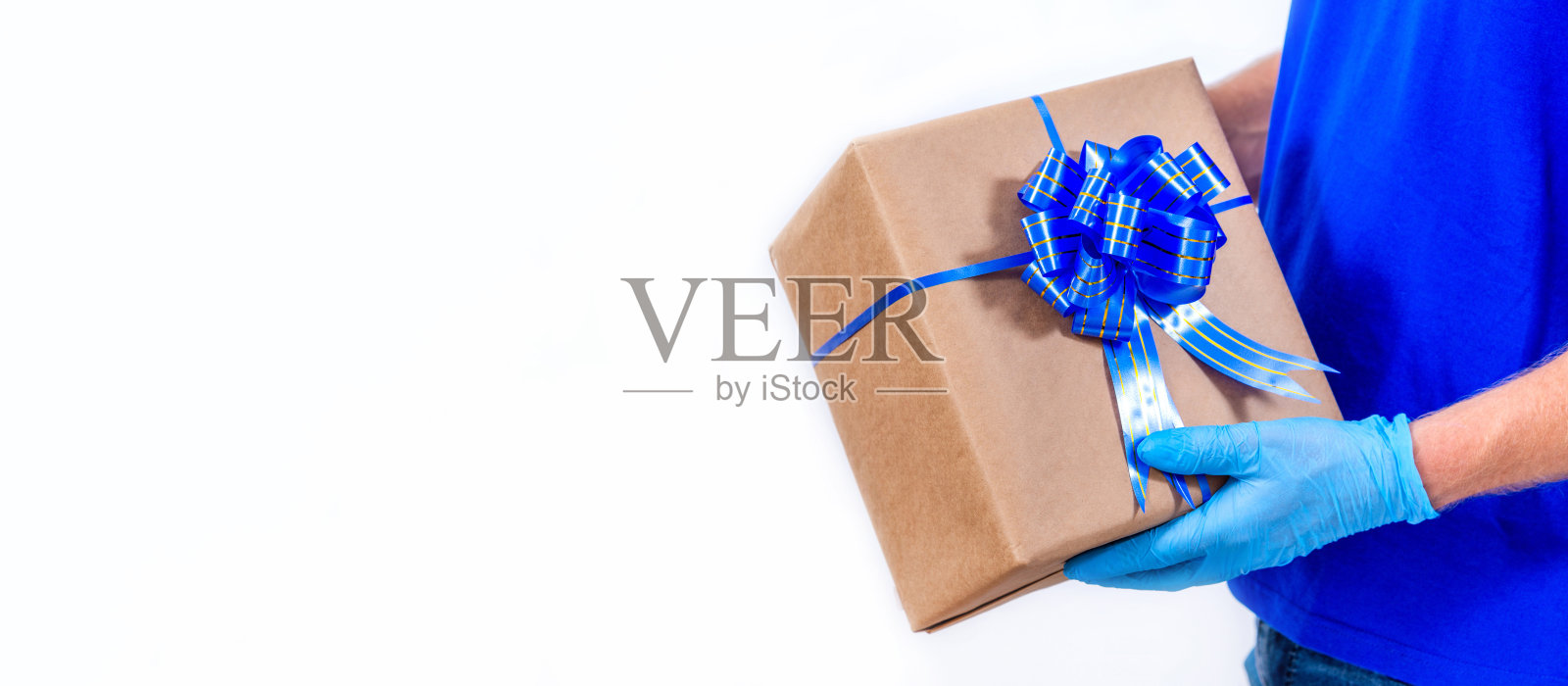 横幅。在冠状病毒大流行期间，安全非接触远程传递节日礼物。快递手在保护医疗手套持有美丽的礼盒与一个蝴蝶结在白色的背景。副本的空间。照片摄影图片