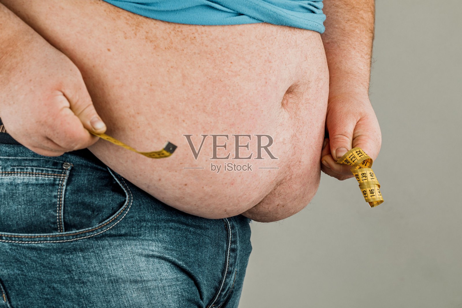 一个男人用卷尺量他的大肚子。在一个灰色的背景。照片摄影图片