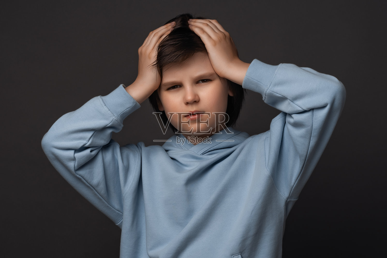 10-12岁男孩压力大，抓住头部的图片。情绪无助。工作室拍摄，灰色背景照片摄影图片