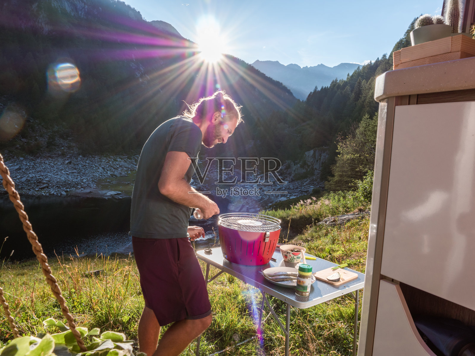 在面包车外用便携式烧烤炉做饭的男人，山景照片摄影图片