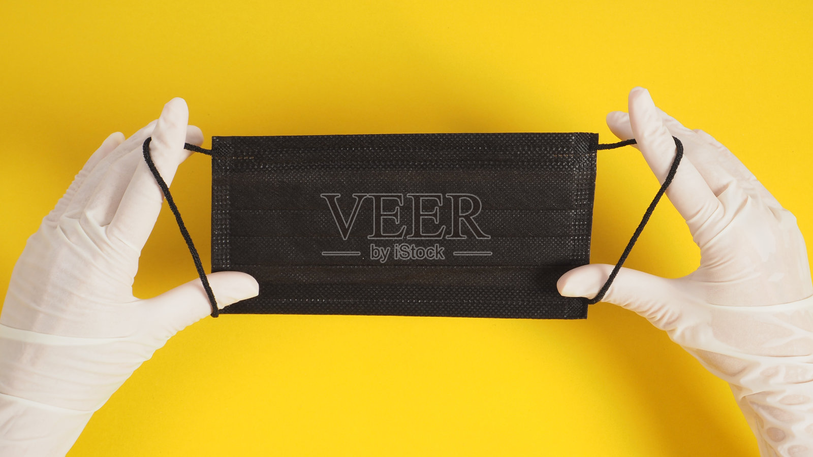 双手戴乳胶手套，黑色面罩，黄色背景。照片摄影图片