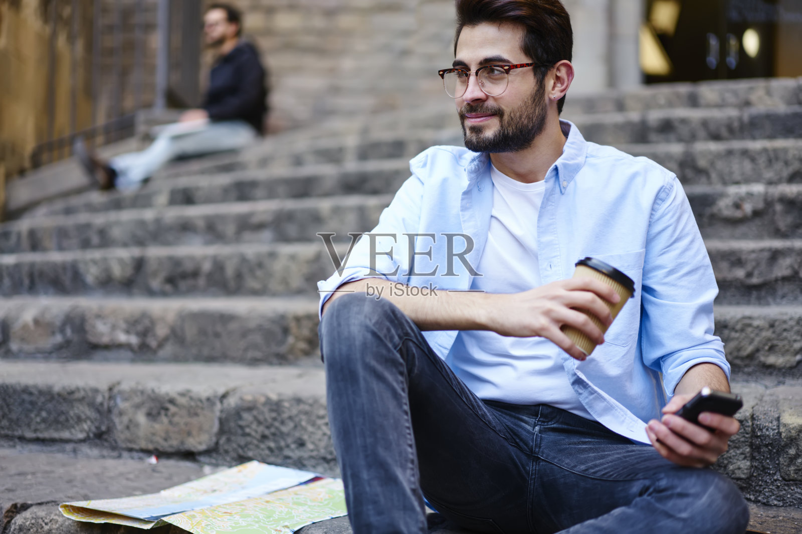 年轻男性游客坐在楼梯上拿着智能手机纸质地图和外卖咖啡照片摄影图片