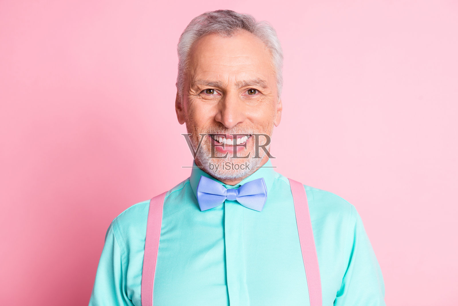 照片肖像的快乐微笑的老人穿着漂亮的衬衫领结和吊带孤立在粉红色的背景照片摄影图片