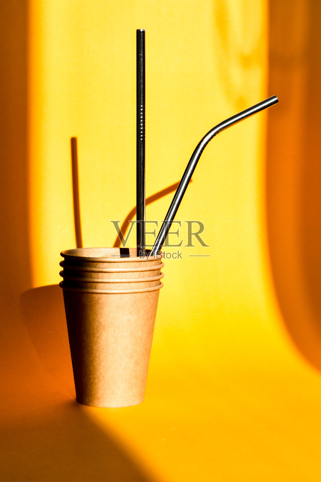 纸制咖啡容器和钢制饮用吸管的背景是黄色的，棕榈叶的阴影很硬。纸杯。塑料是免费的。“零浪费”照片摄影图片