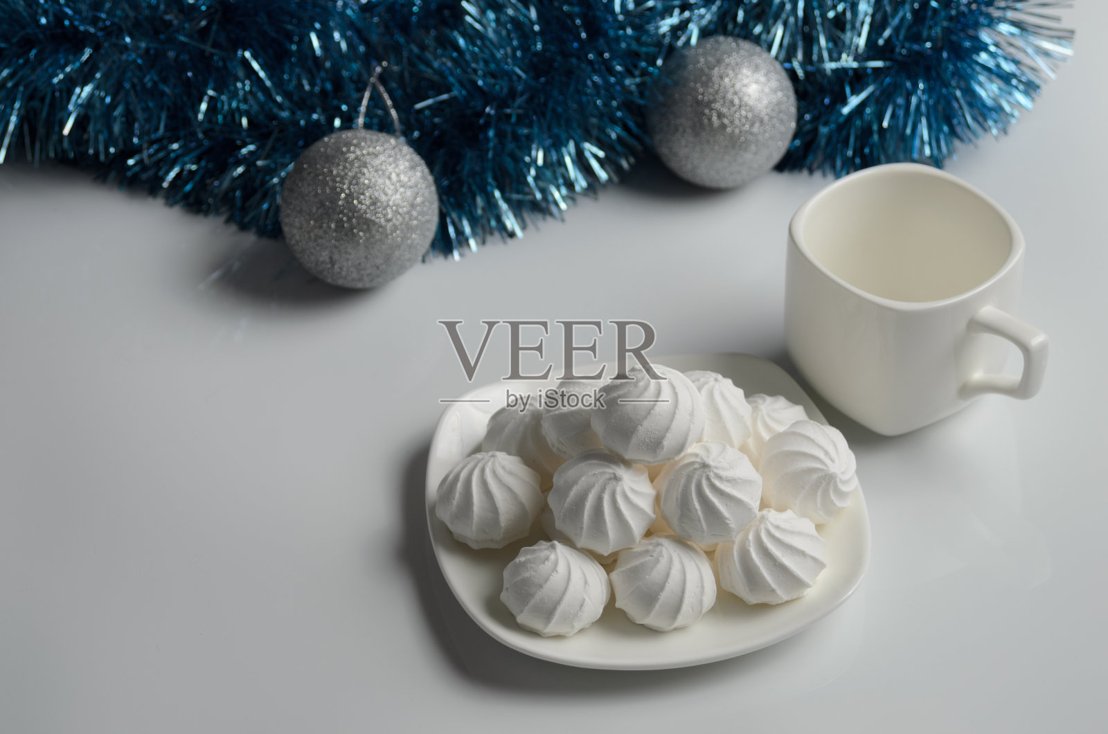 在圣诞装饰的背景上，盘子里放着几块蛋白酥皮和一杯茶。照片摄影图片