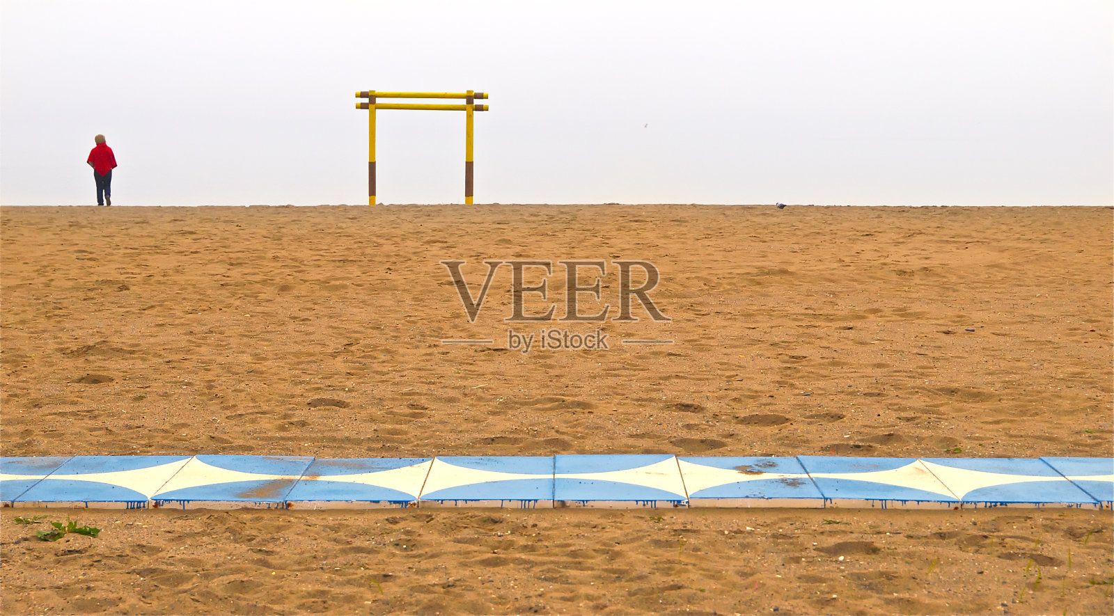 在一个孤独的海滩上，穿着红色大衣的女人照片摄影图片