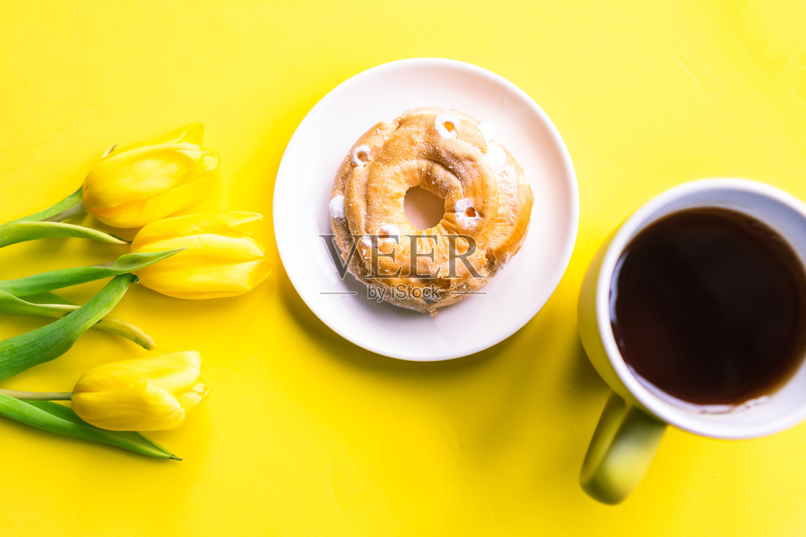 甜美可口的甜甜圈，郁金香和咖啡杯在桌子上，黄色的背景，俯视图照片摄影图片