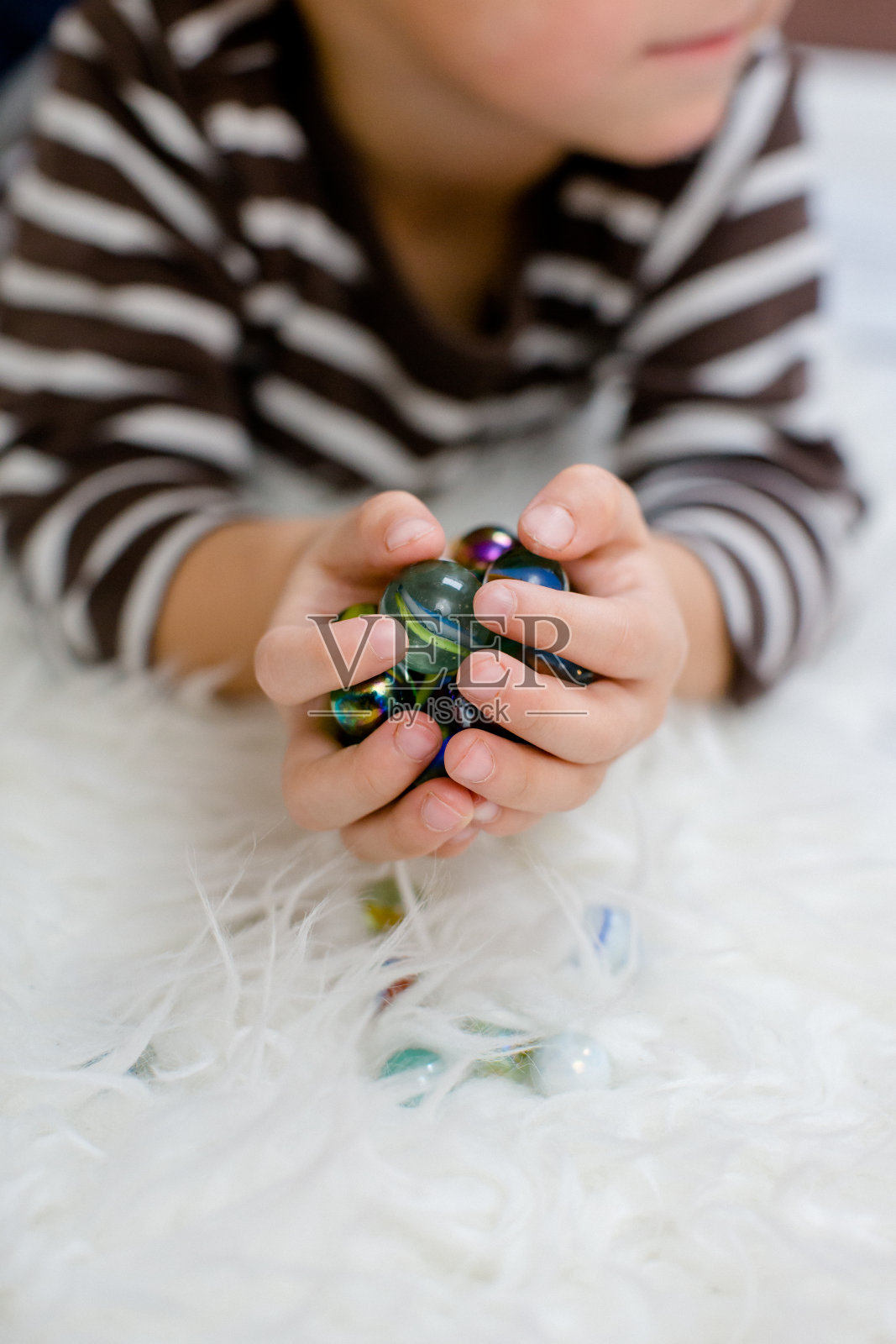 蹒跚学步的孩子手里拿着许多大理石，躺在地板上照片摄影图片