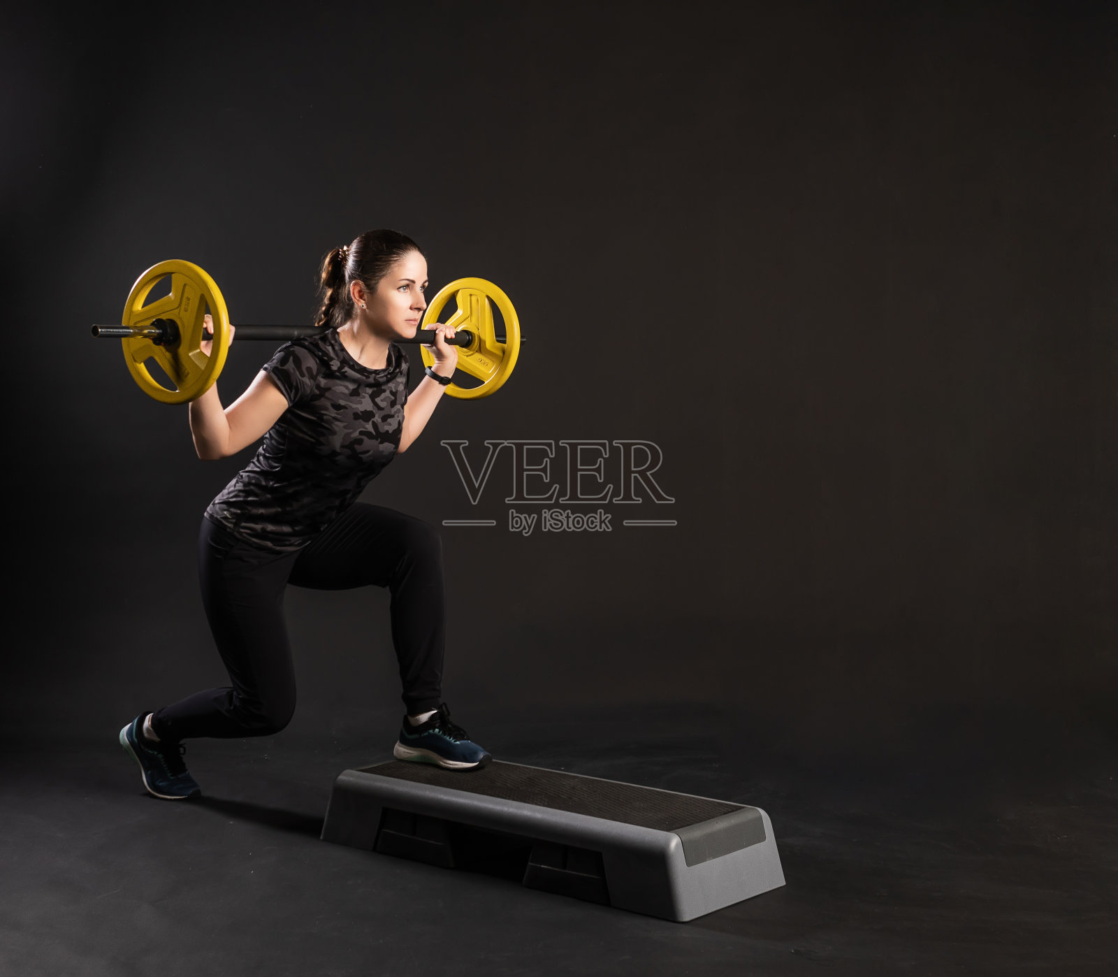 健身女在台阶台上，拿着杠铃，黄煎饼放在吧台上做运动。黑色背景下的运动真漂亮照片摄影图片