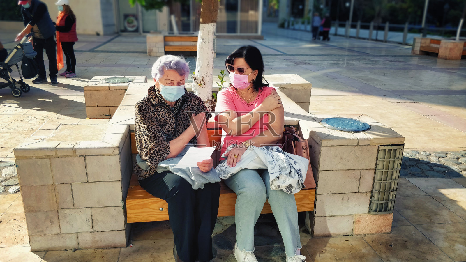 女儿和年迈的母亲一起接种了流感疫苗。接种疫苗后，她们在医疗中心旁边的长椅上等待了15分钟。由于疫情，两人都戴着口罩。照片摄影图片