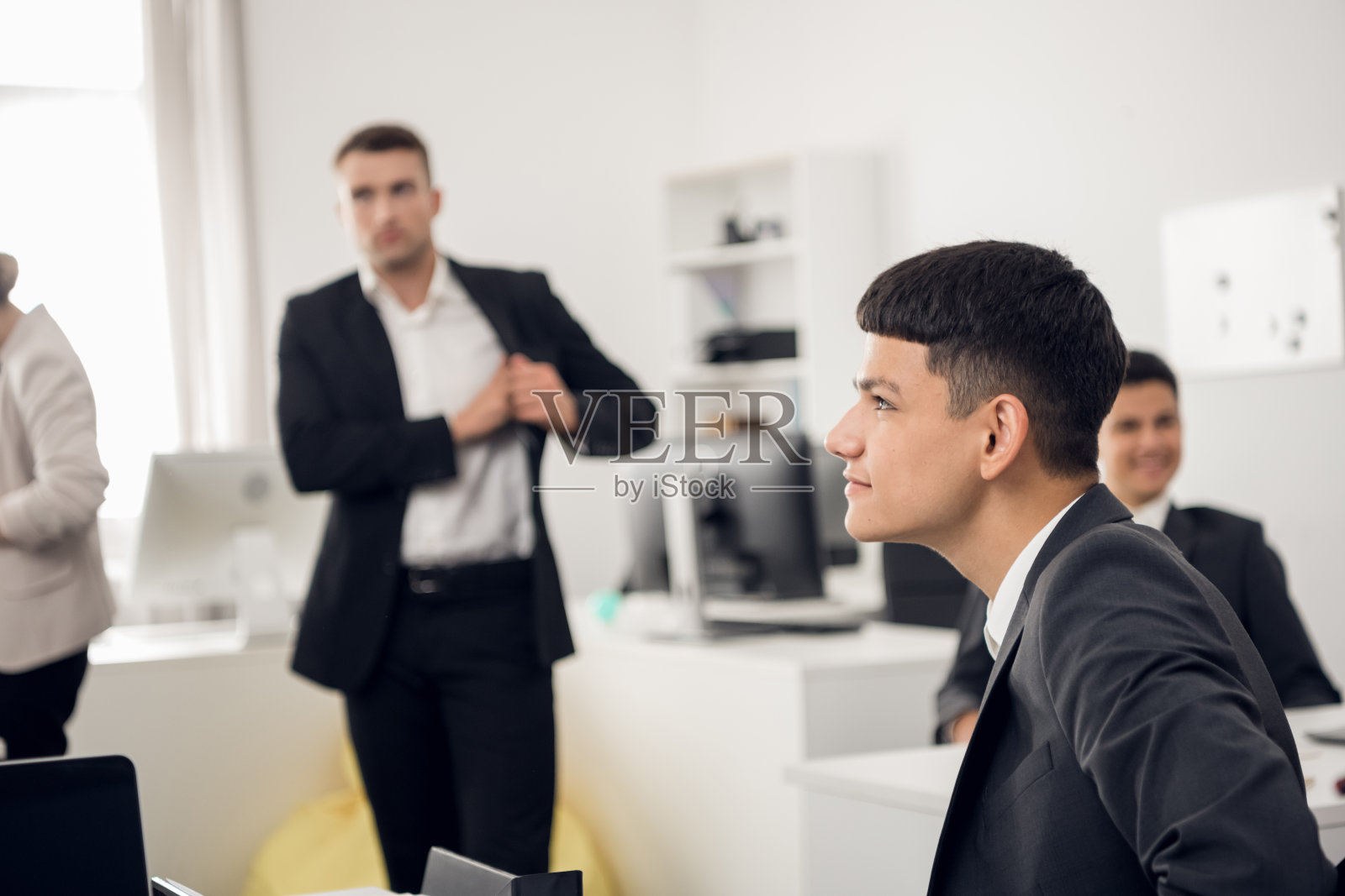 一个正在发展中的公司的年轻员工在明亮的办公室里微笑的前景。背景是正在吃午饭的同事照片摄影图片