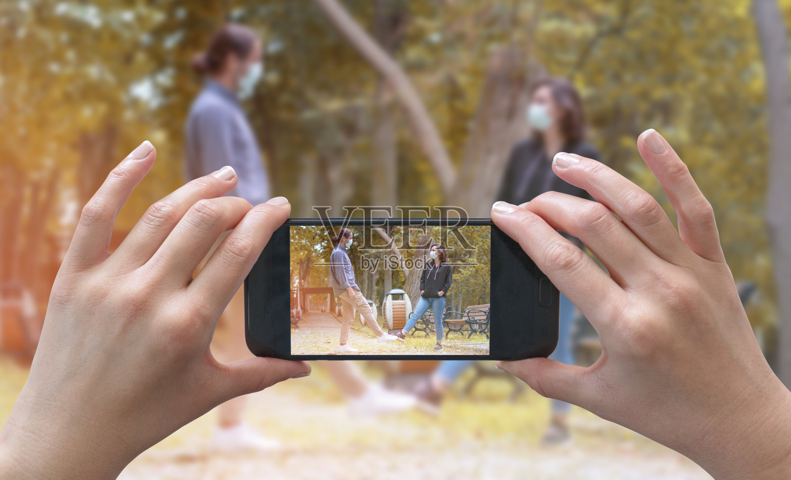 女性用智能手机拍照，年轻快乐的朋友，模糊的背景，covid-19 consep。一名女性拍摄covid-19非接触问候。照片摄影图片