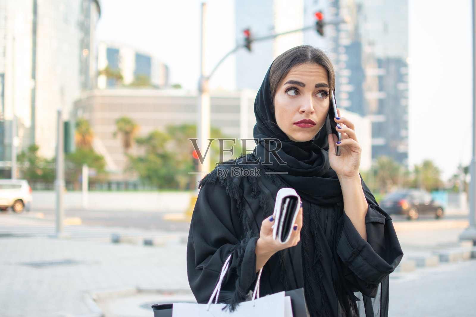 在街上打电话、拿着钱包和购物袋的穆斯林妇女照片摄影图片