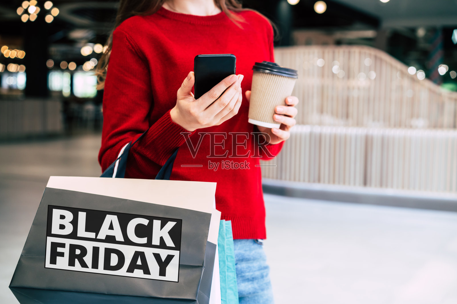 在黑色星期五这天，漂亮时髦的年轻女子拿着五颜六色的购物袋，心情很好地拿着智能手机和信用卡走在商场里照片摄影图片