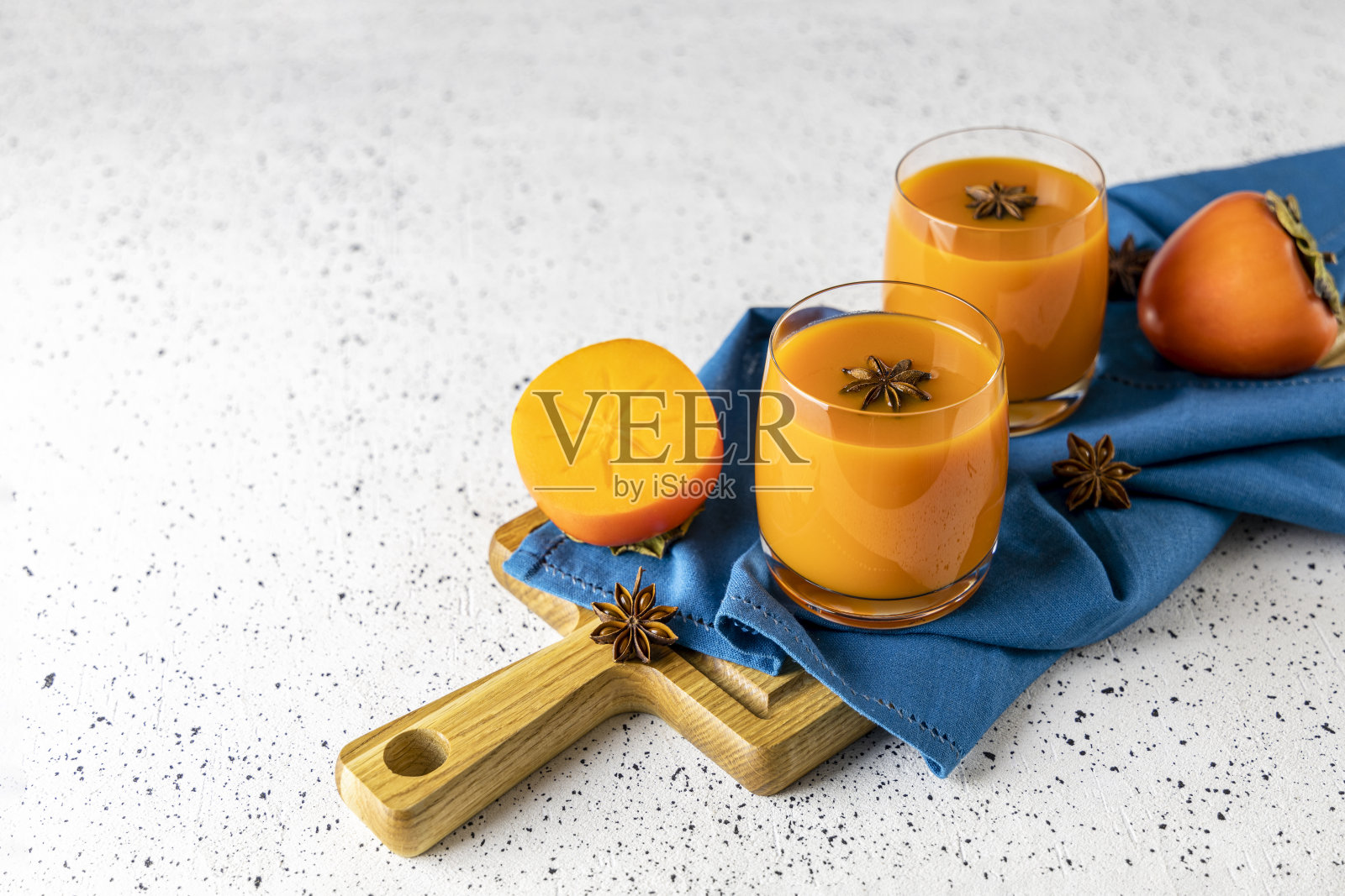 两杯新鲜健康的柿子冰沙配八角放在切好的木板上，灰色的混凝土背景照片摄影图片