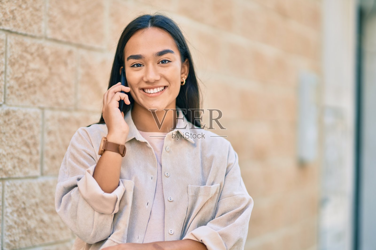 年轻的拉丁女孩开心地在城市里用智能手机聊天。照片摄影图片