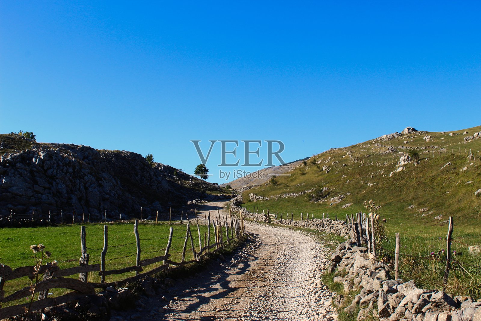 秋天在山上。这条路被石头和木柱包围着，柱子之间用带刺的铁丝连接。这条山路通向古老的波斯尼亚村庄Lukomir。Bjelasnica山。照片摄影图片