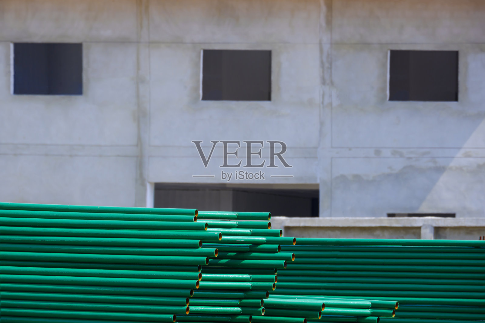 在建筑施工现场区域，许多绿色金属屋面结构桩位于建筑结构前的地板上照片摄影图片