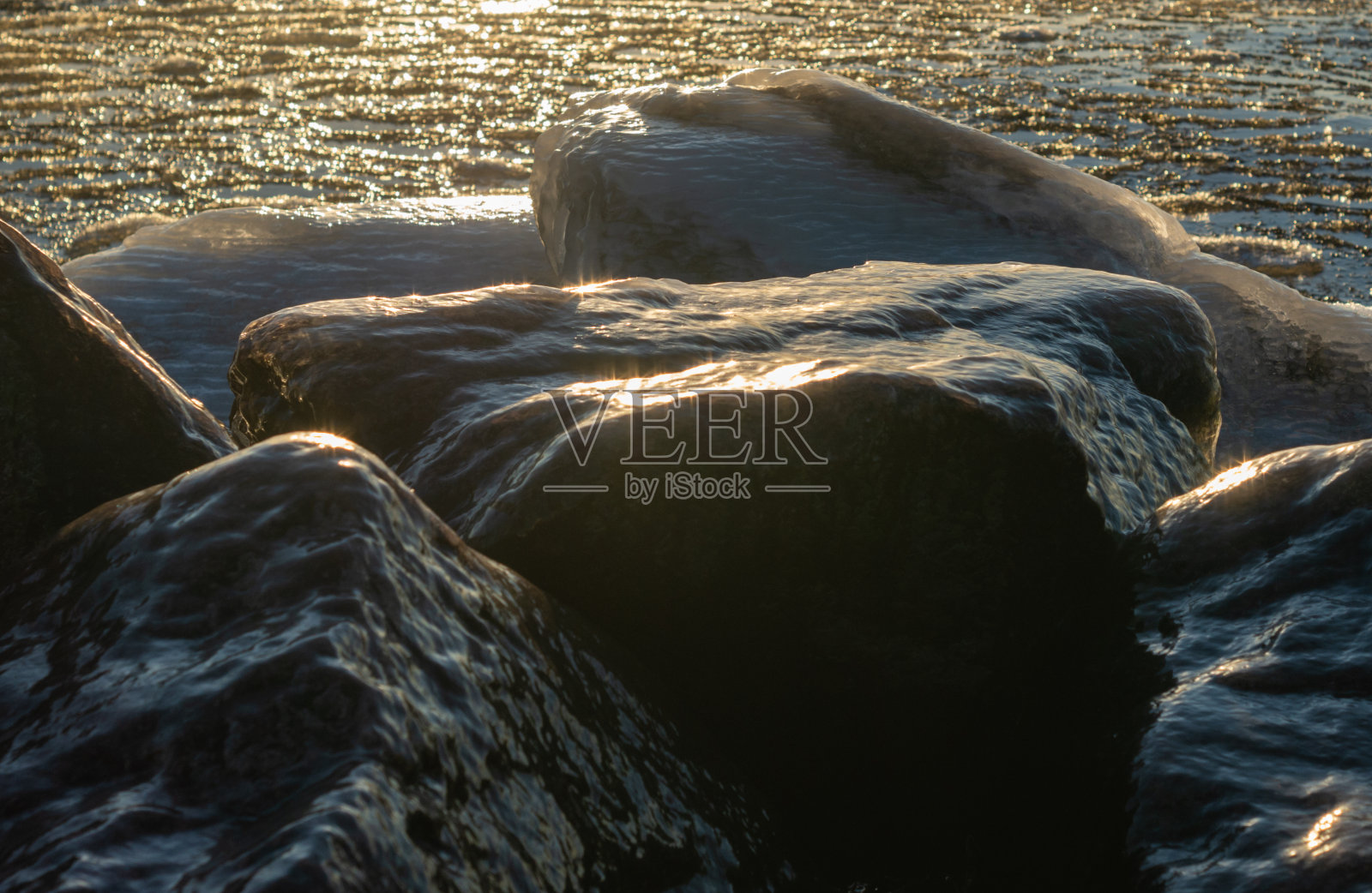 海滩上冰冻的岩石。在冬天日落。照片摄影图片