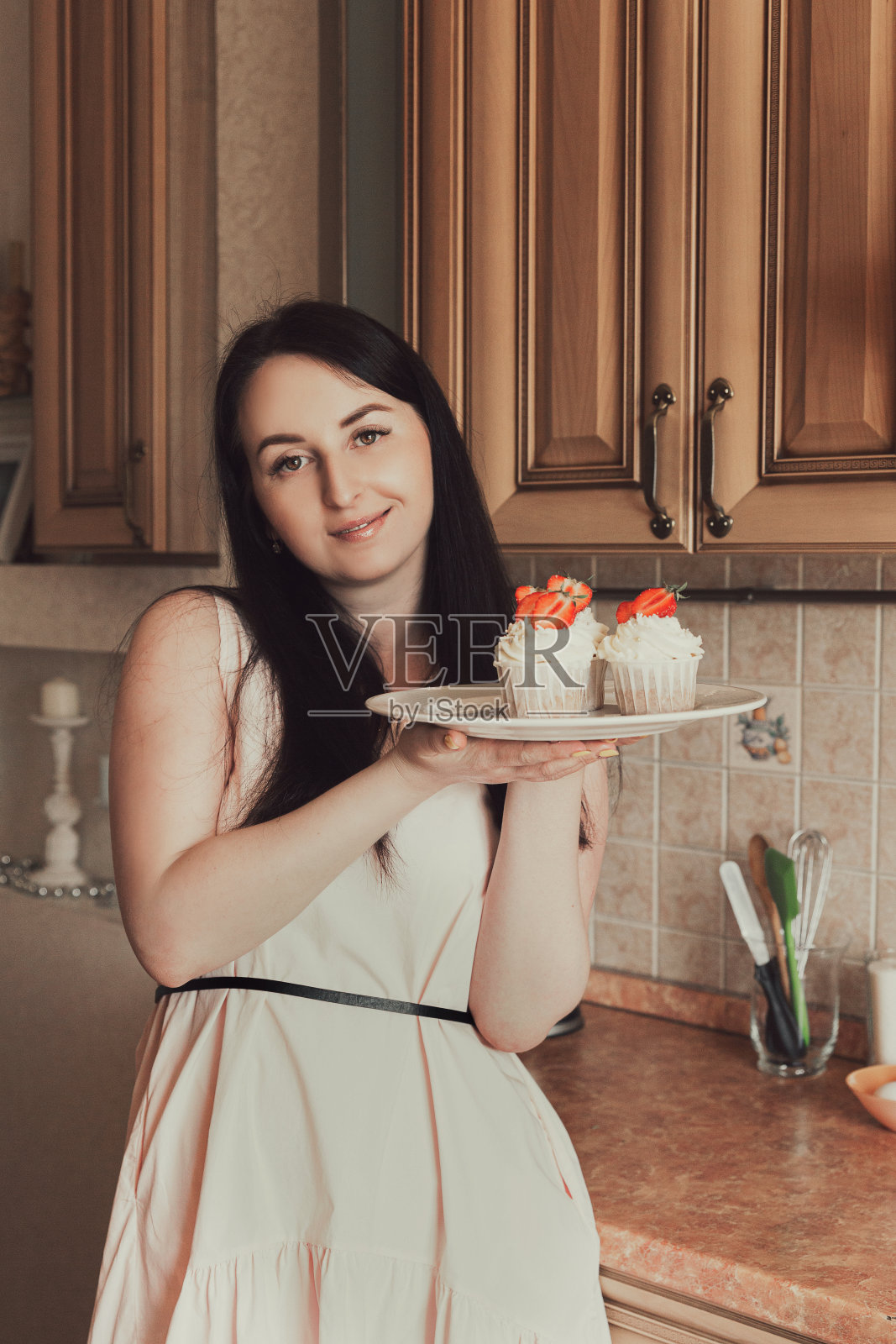 一个粉色裙子的女人手里拿着装饰着草莓的白色奶油纸杯蛋糕照片摄影图片