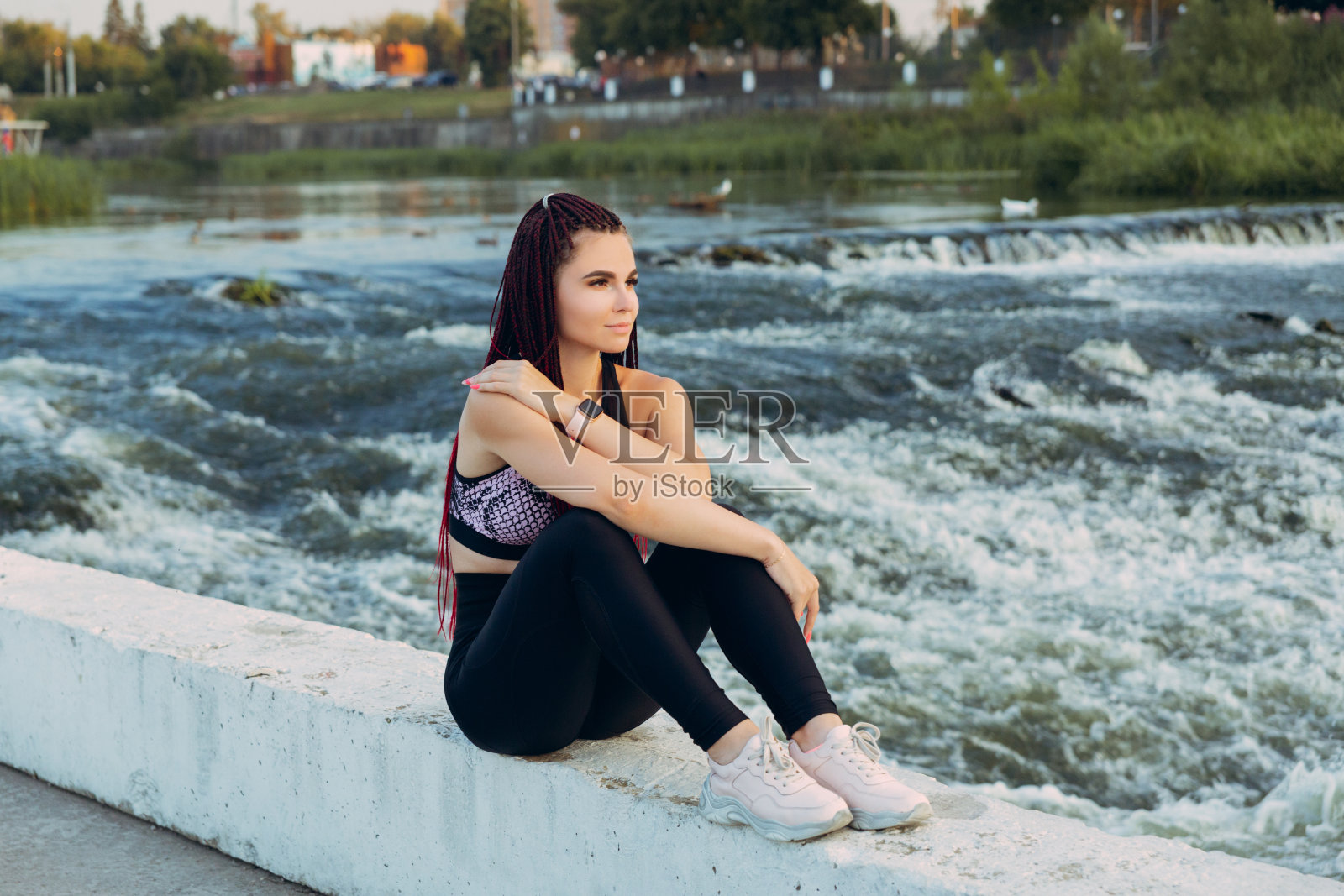 一位梳着许多辫子的年轻女子穿着运动服，坐在湍急的河流中照片摄影图片