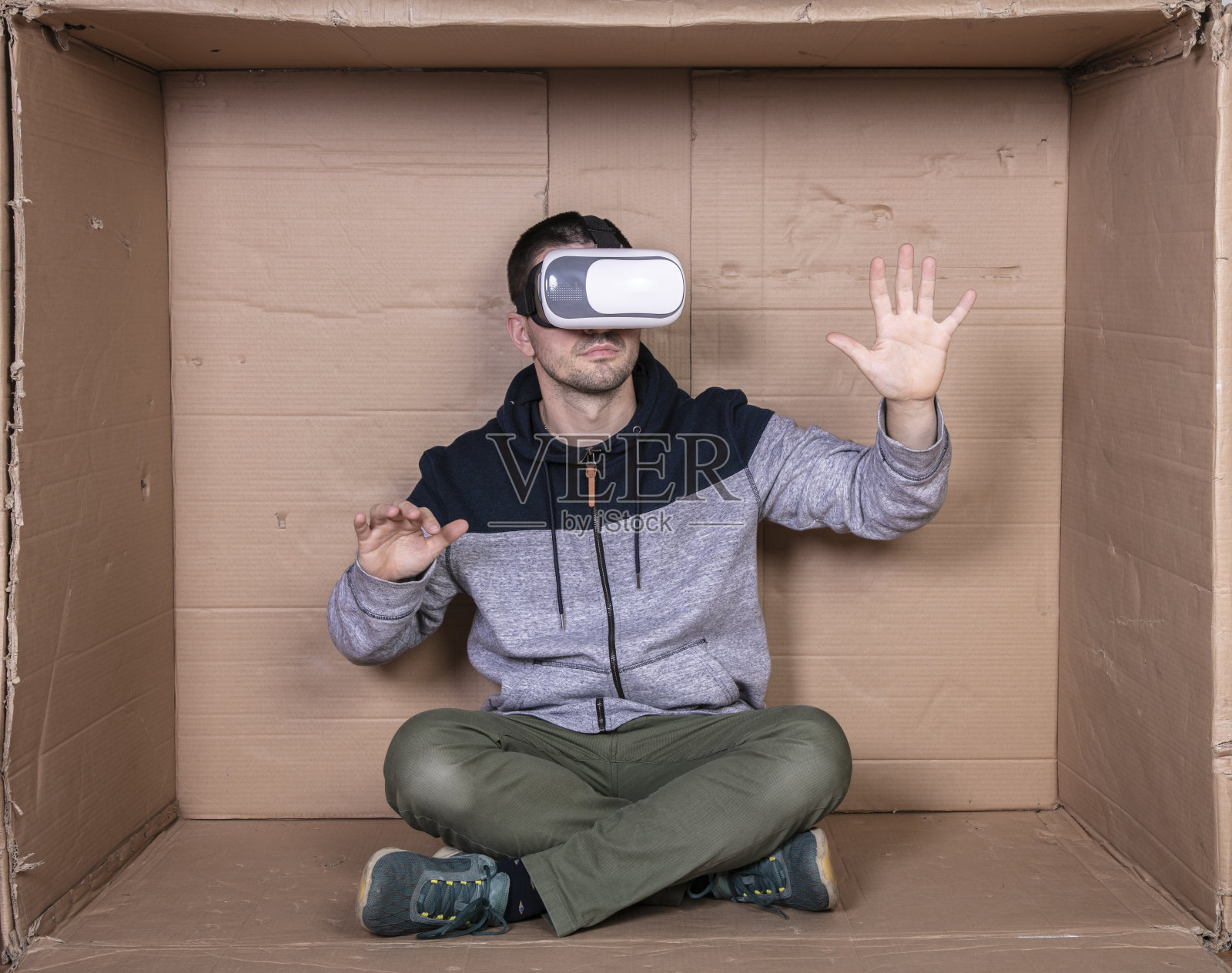 戴着虚拟现实眼镜的人，坐在硬纸板房间里娱乐照片摄影图片