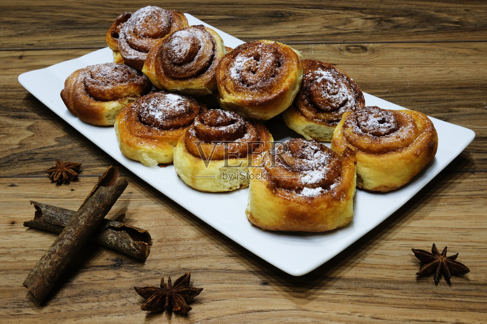 在长方形盘子上撒上糖粉的肉桂卷。照片摄影图片