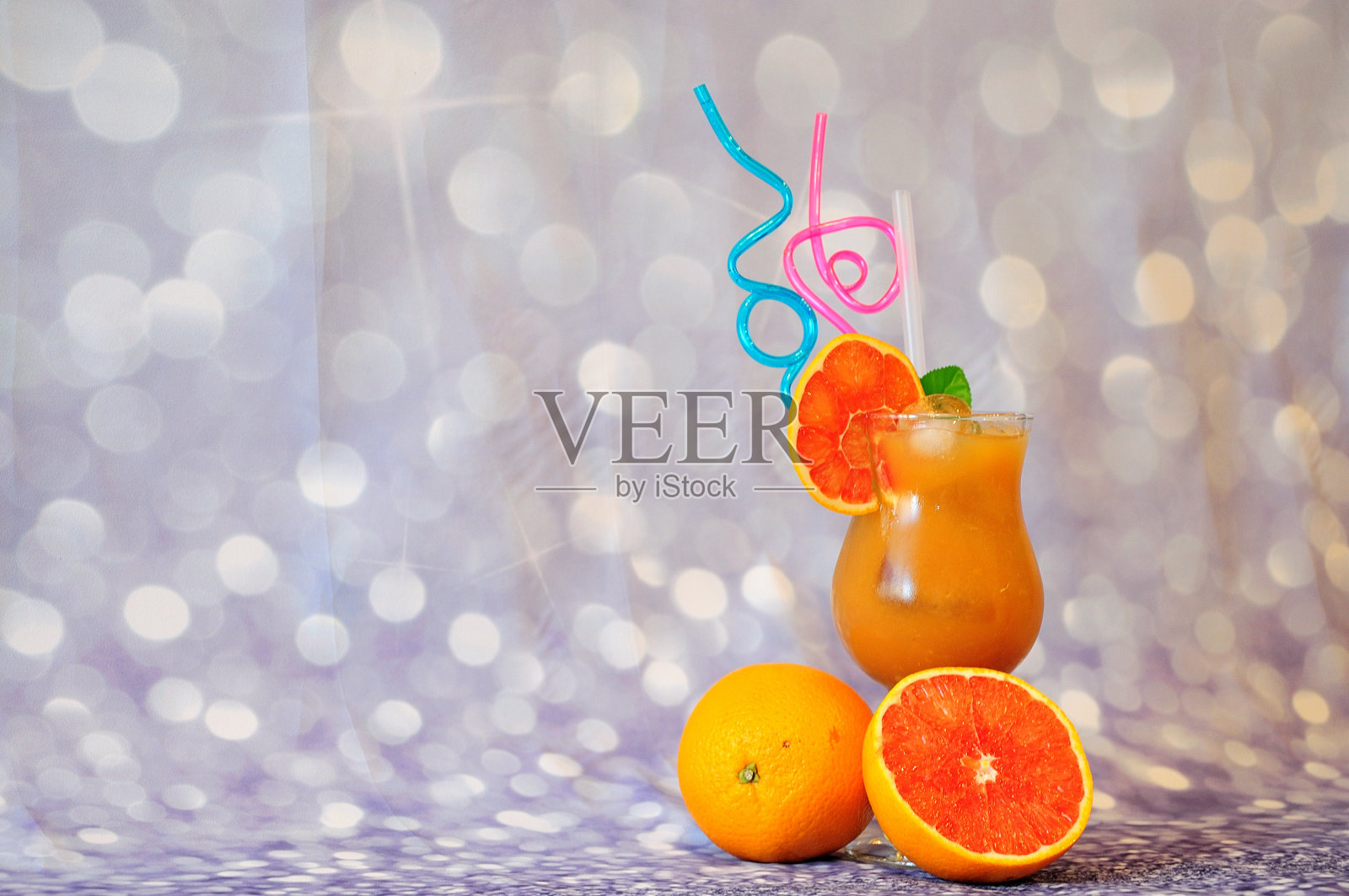 在灰色抽象的背景上，一杯有冰的柑橘汁和成熟的柚子水果。照片摄影图片