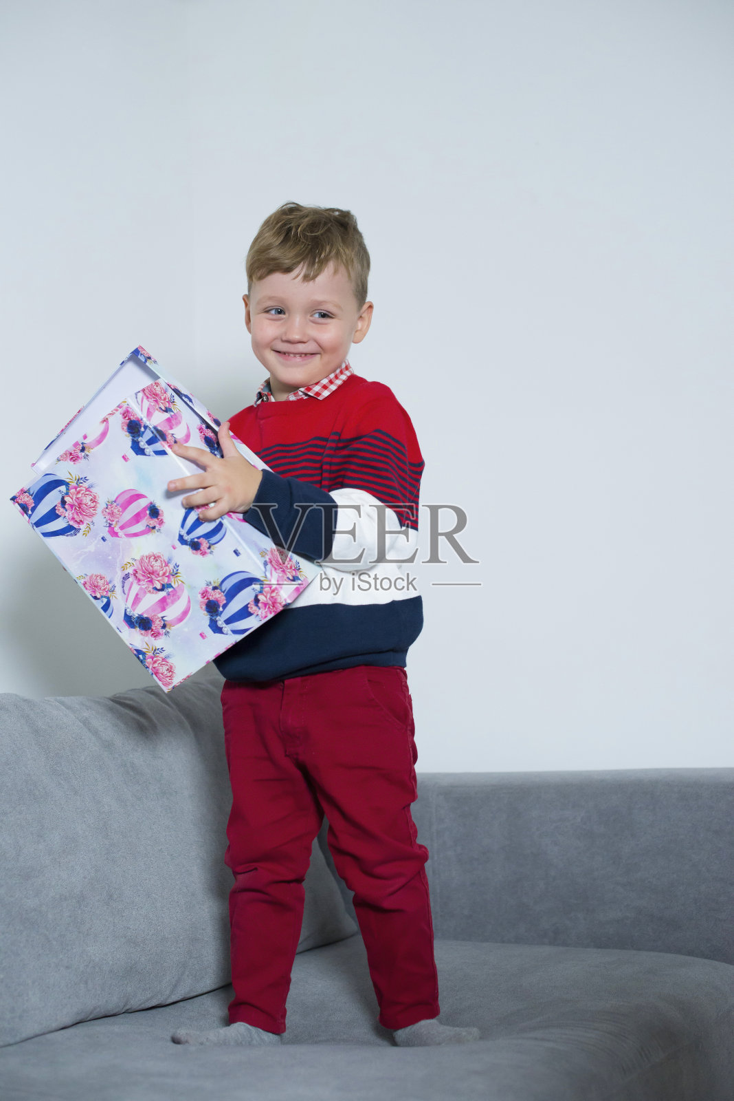 男孩微笑着，手里拿着一个大礼物。照片摄影图片