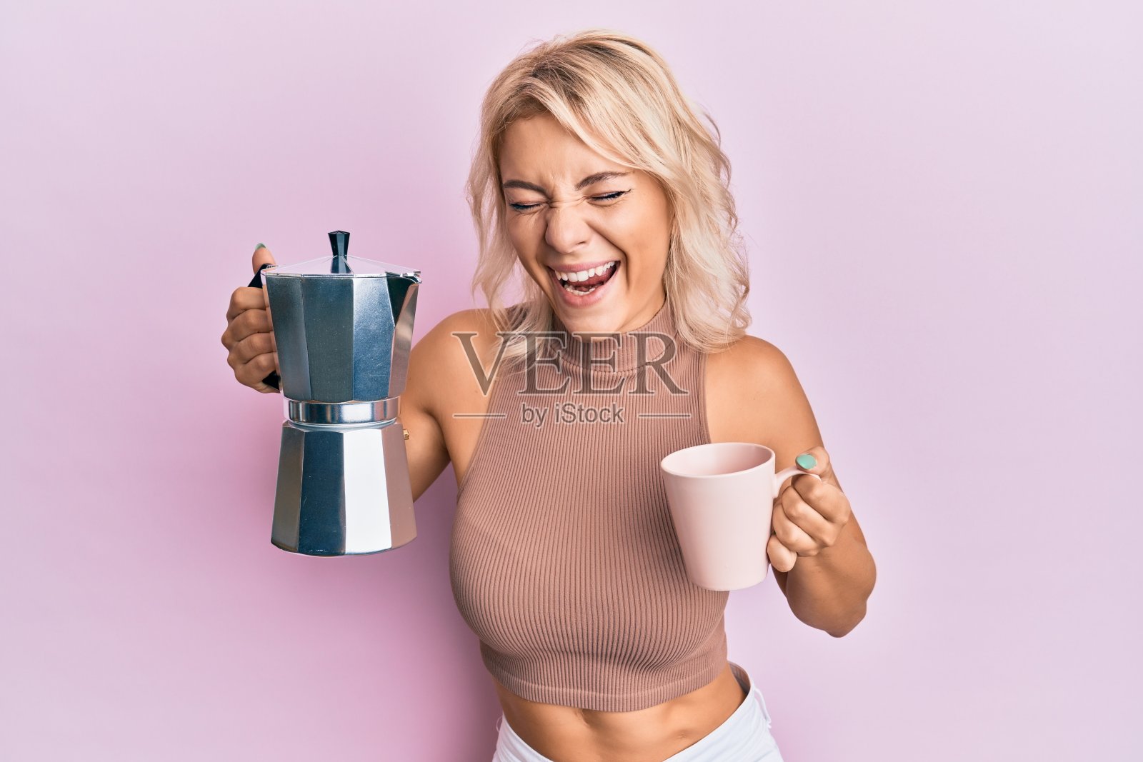 年轻的金发女孩喝意大利咖啡，笑得很大声，因为有趣的疯狂笑话。照片摄影图片