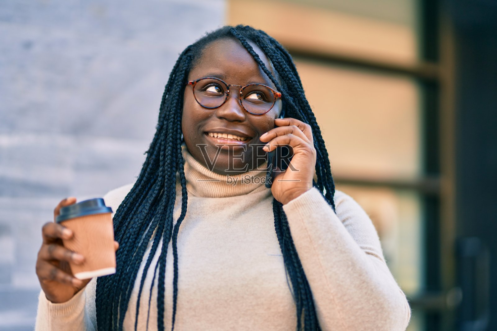一位年轻的非裔美国女性一边用智能手机聊天一边喝着城市里的外卖咖啡。照片摄影图片