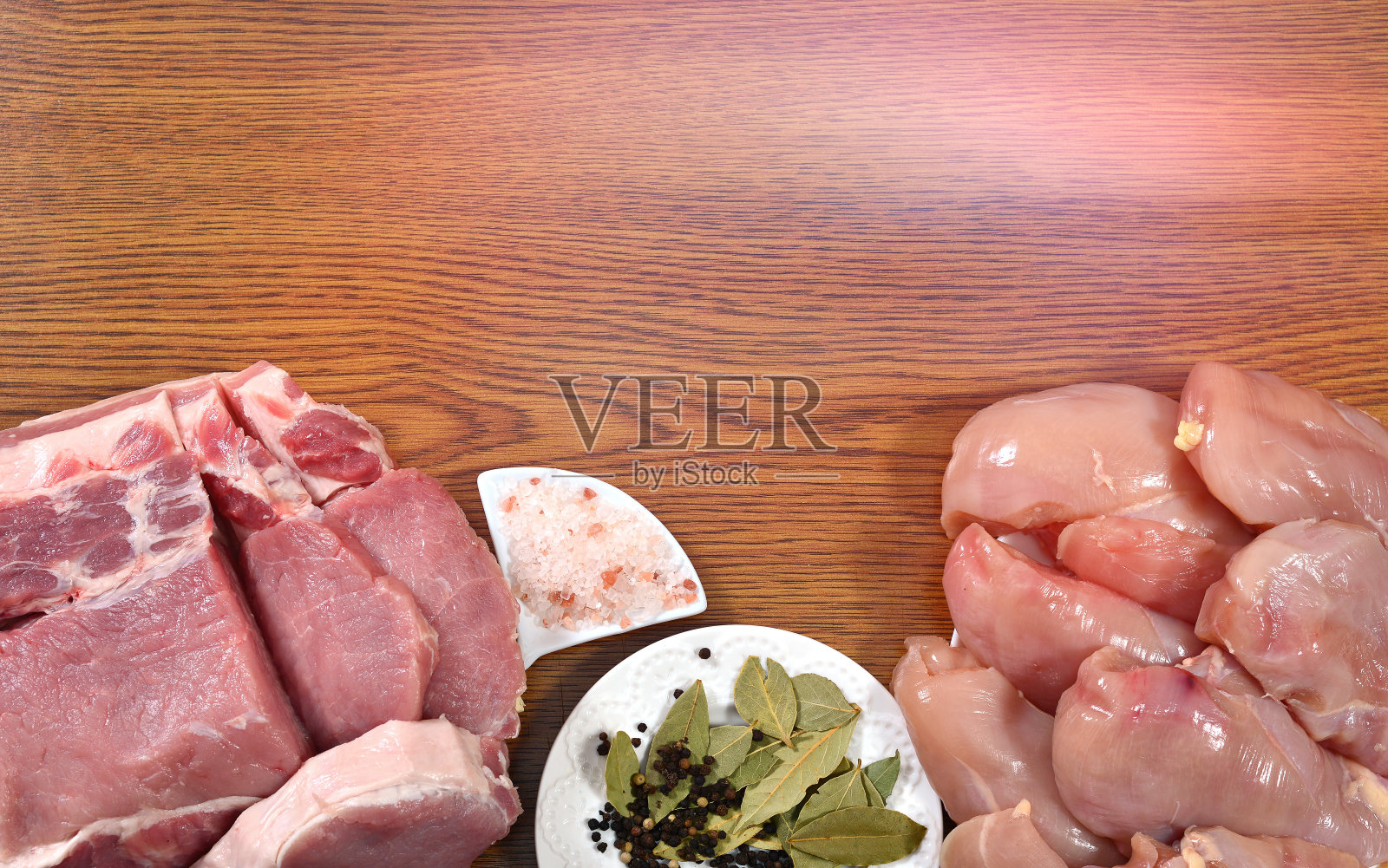 生鸡柳，猪肉片，一盘月桂叶，胡椒，香料，盐放在木头背景的桌子上，粉红色的灯光从上面照射下来。照片摄影图片