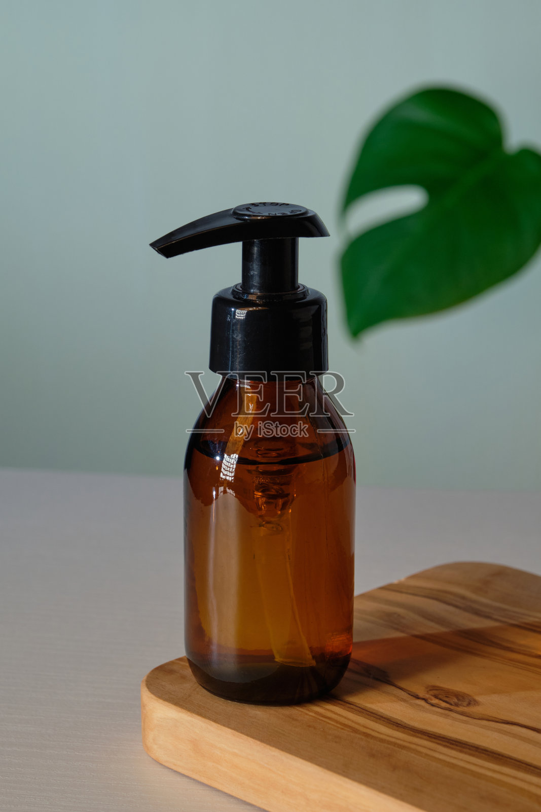 透明琥珀色玻璃泵瓶模型与热带绿叶。天然有机化妆品分配器包装设计。照片摄影图片