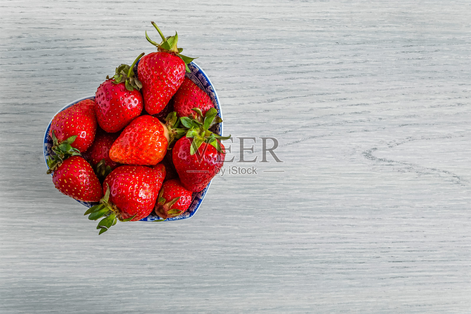 心形的碗，满是草莓，放在浅色的木质背景上。照片摄影图片