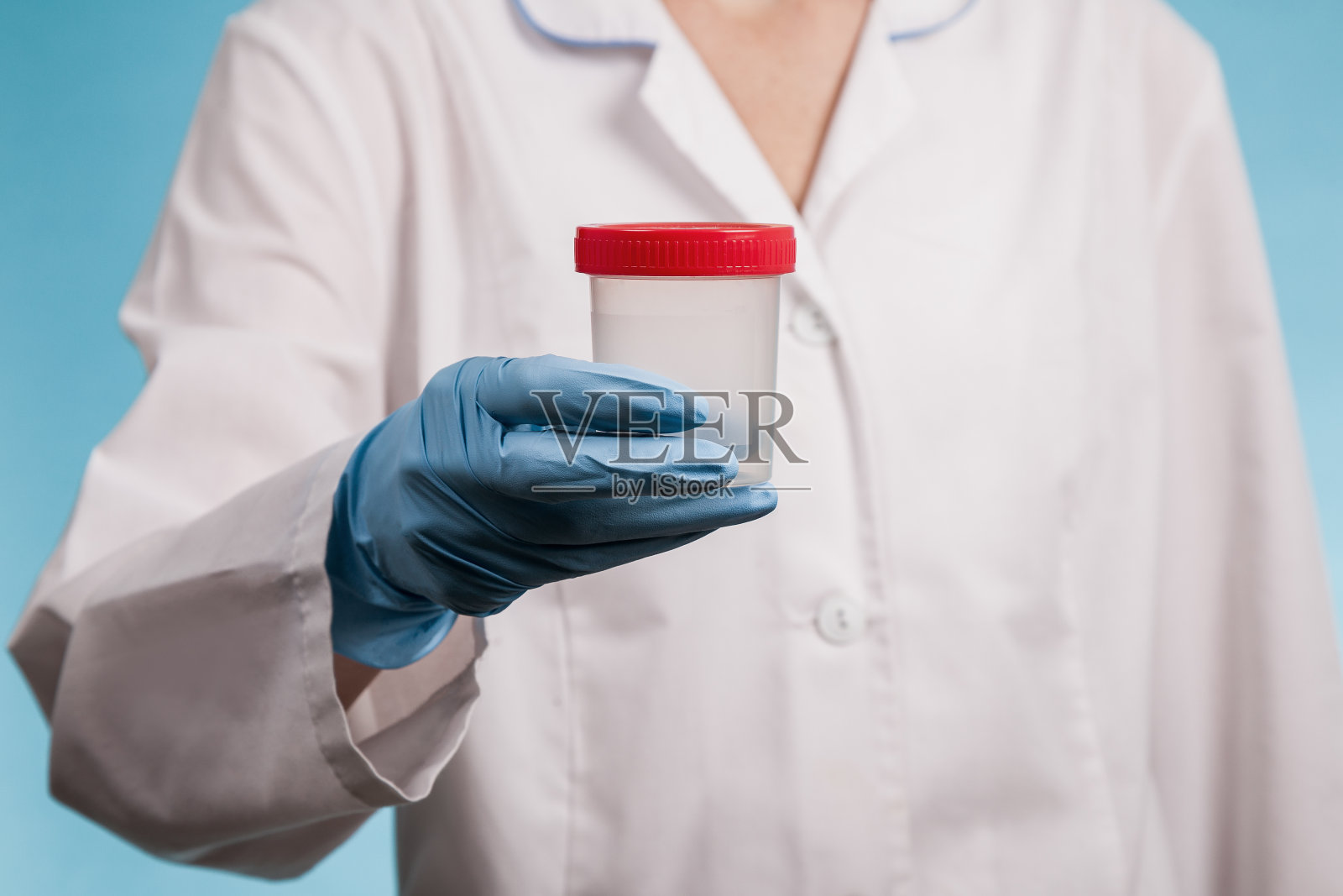 医生身穿白色制服，蓝色背景上戴着蓝色手套，手里拿着一个空的塑料测试瓶照片摄影图片