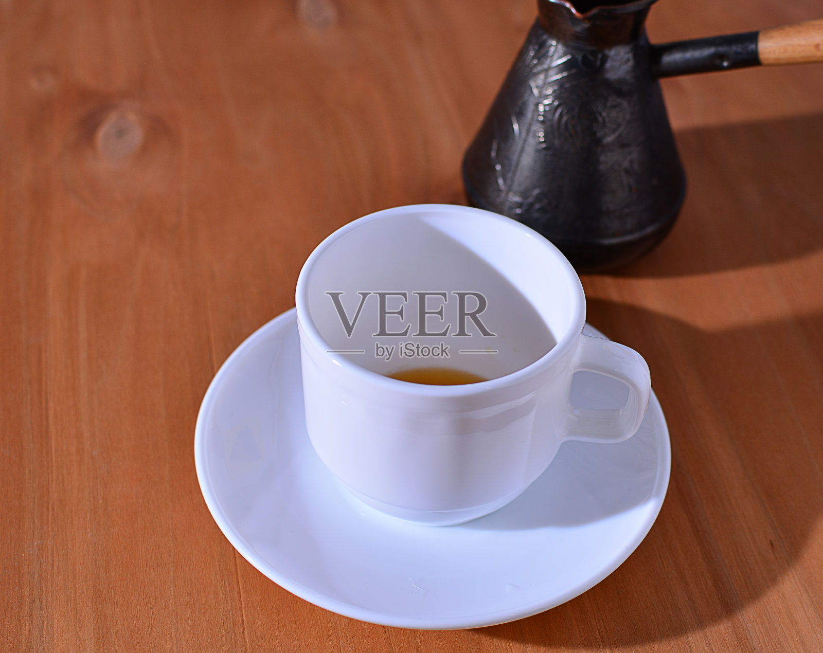 热咖啡从土耳其倒进一个白色的杯子，木制背景。照片摄影图片