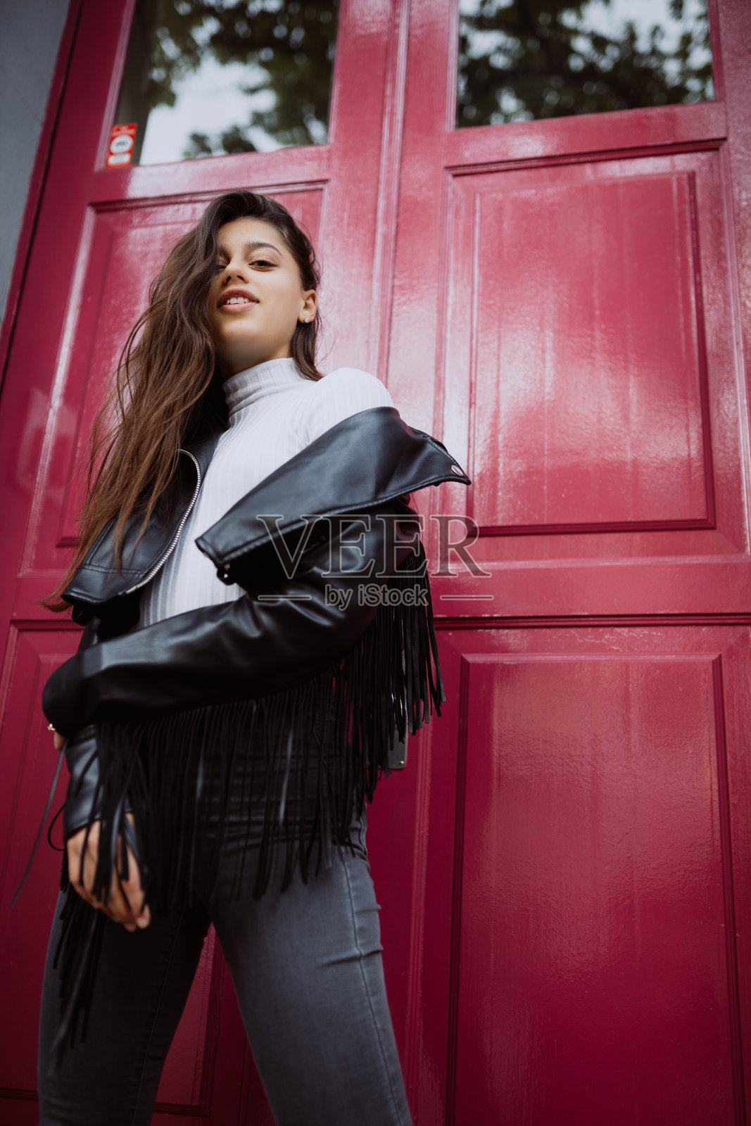 一个年轻女人站在外面一扇红色的门旁边照片摄影图片